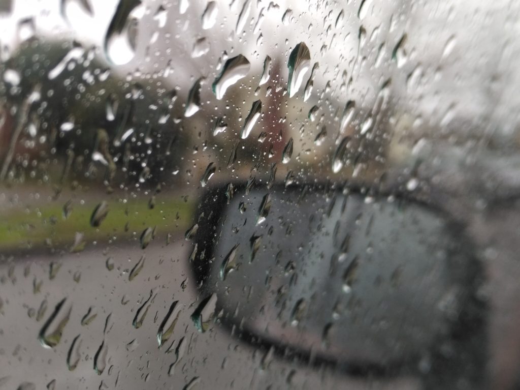 Raindrops on a car window. Behind, a view of a residential street, out of focus.