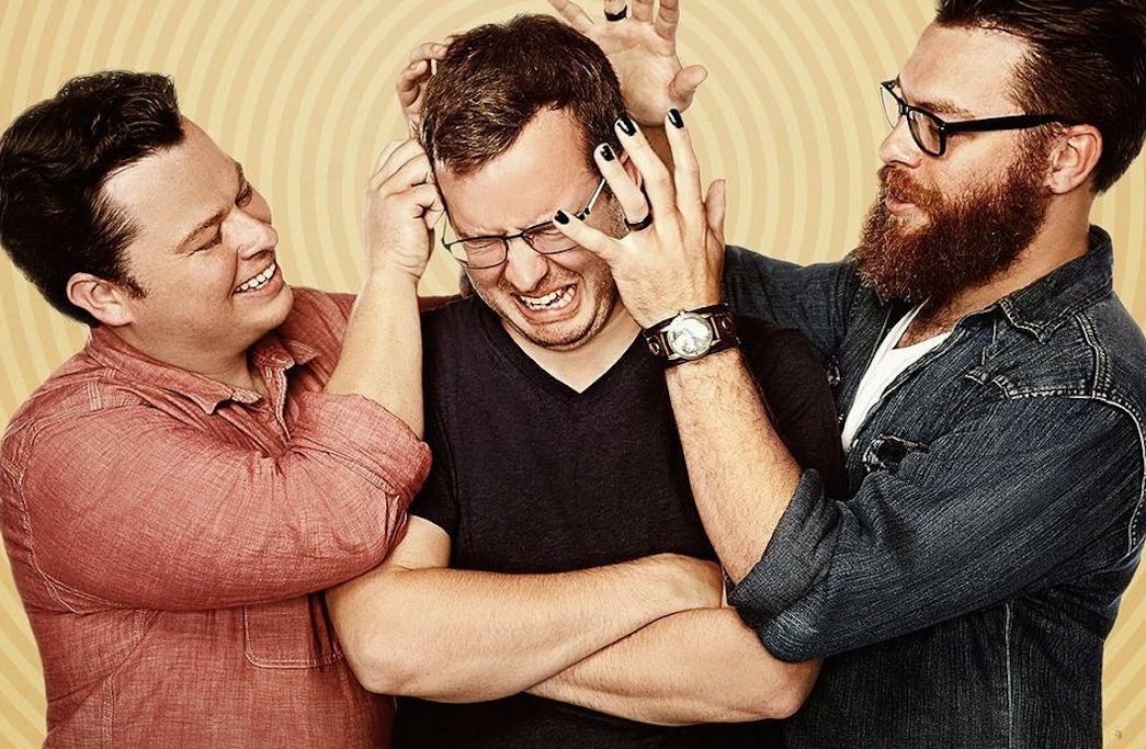 The three McElroy brothers. Travis and Justin are standing on either side of Griffin and messing with his hair.
