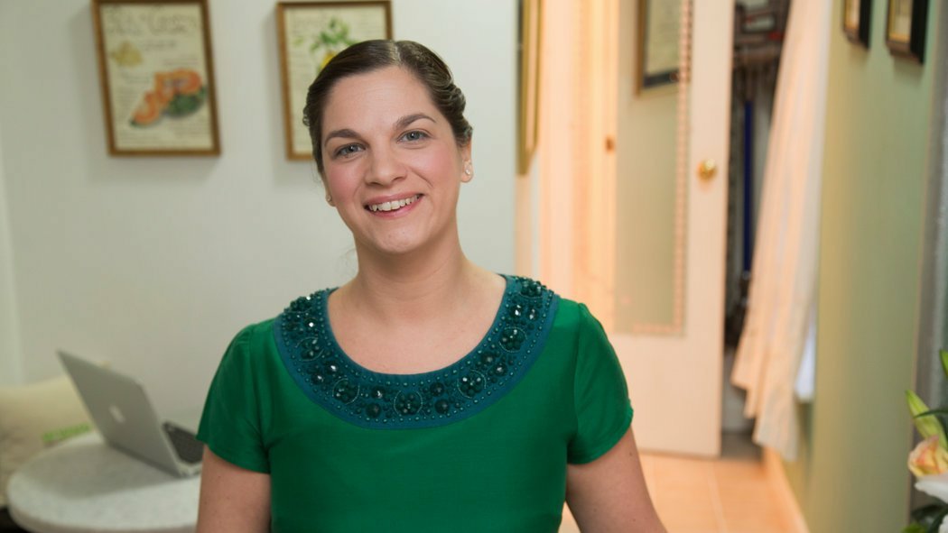 A photo of Jolie Kerr standing in a clean bedroom, smiling at the camera.