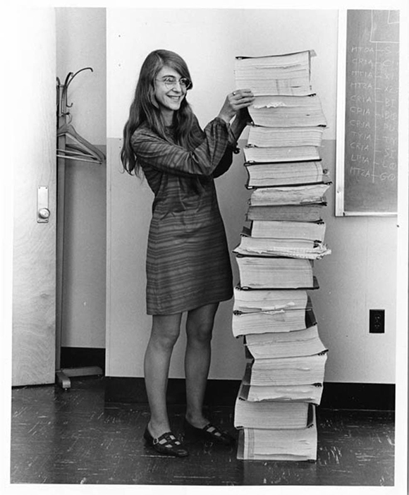 NASA engineer Margaret Hamilton standing next to a stack of binders containing her program's results. The stack is as tall as she is.