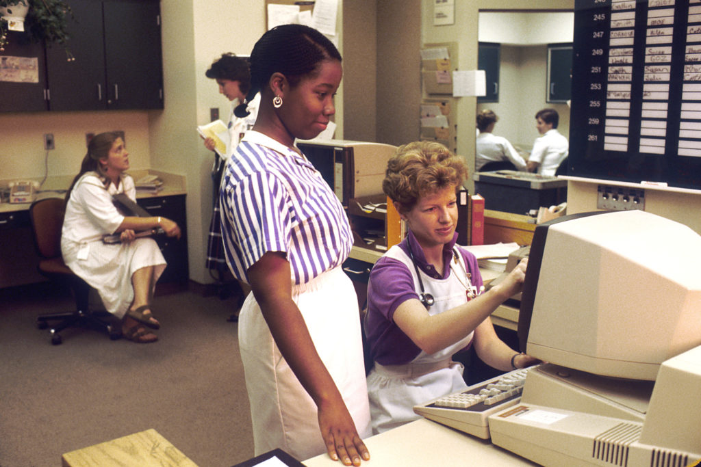 Two nurses working at a computer in a nursing station in 1987.