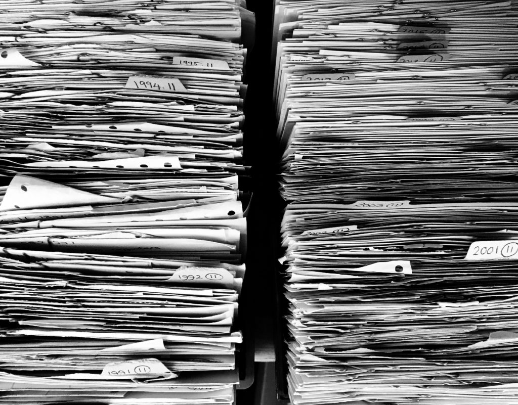 A close up, black and white image of two stacks of folders, files, and paper, with a small gap between them. They reach up past the top of the photo.