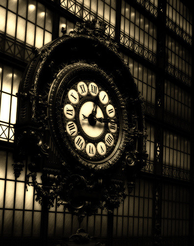 A large clock, with its numbers written in roman numerals, built into the side of a building. It is at least two stories tall. A still from the movie Dark City (1998).