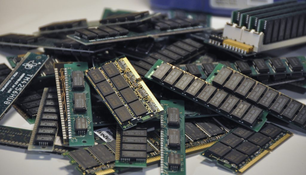 A pile of various computer RAM DIMMs on a white surface.