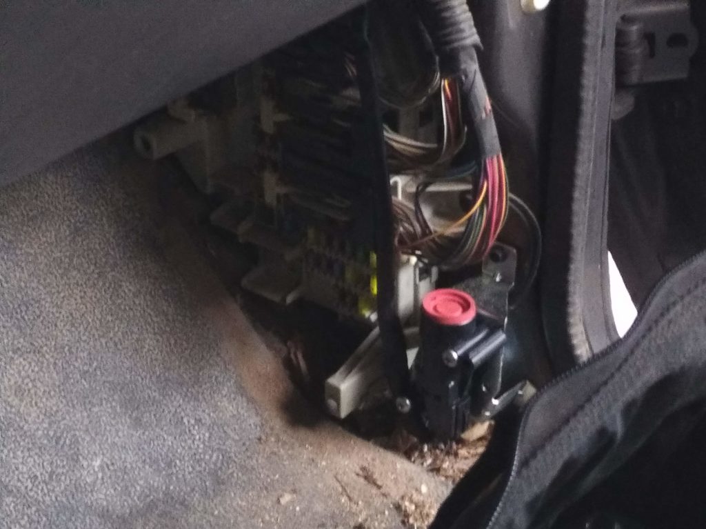 The footwell of the passenger side of a 2006 Ford Ranger. Visible is the fuel interrupt reset button and the fuse panel. The interior plastic panels have been removed. On the fuel interrupt reset is a big red button.