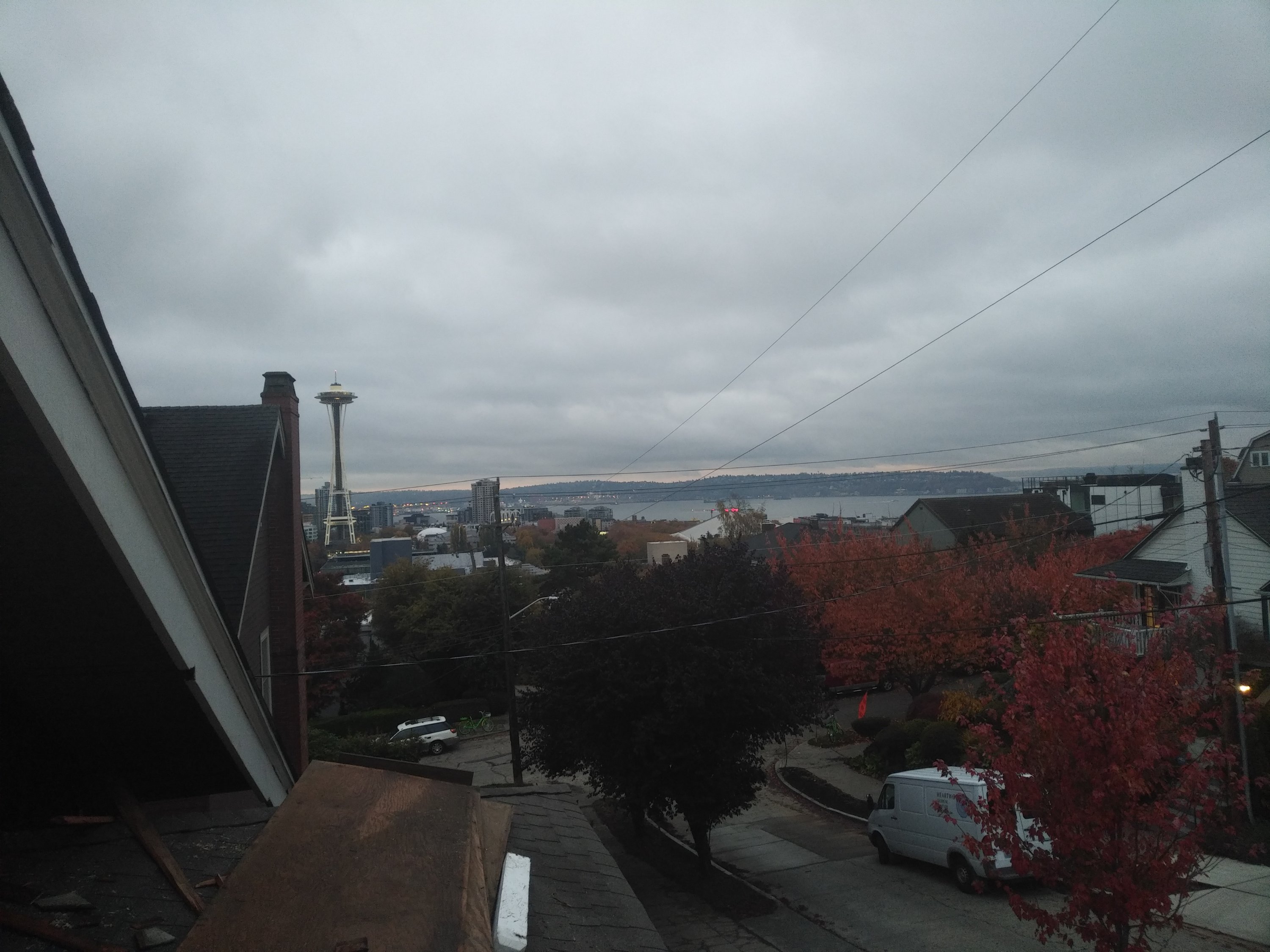 A view from a house rooftop overlooking Seattle. The space needle, the sound, and several large buildings are visible. The sky is covered by grey rainclouds.