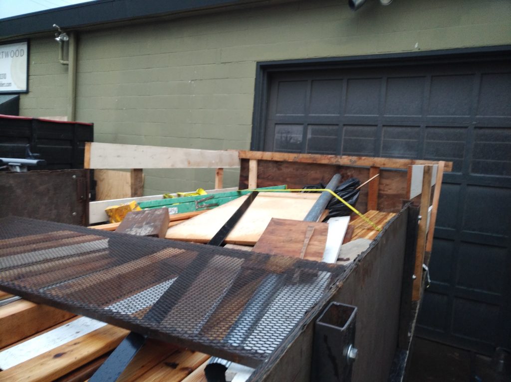 A flatbed truck with side and back walls attached, full of lumber and junk. The back wall and the rearmost sidewalls are made from scrap lumber.