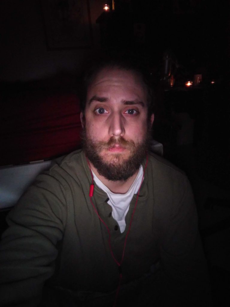 The author squinting slightly at the camera and looking tired while in a dark room.