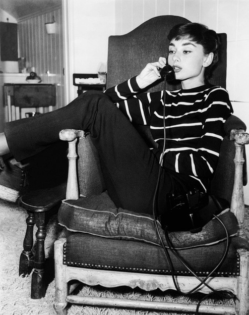 Audrey Hepburn sitting in a chair, talking into a landline phone.