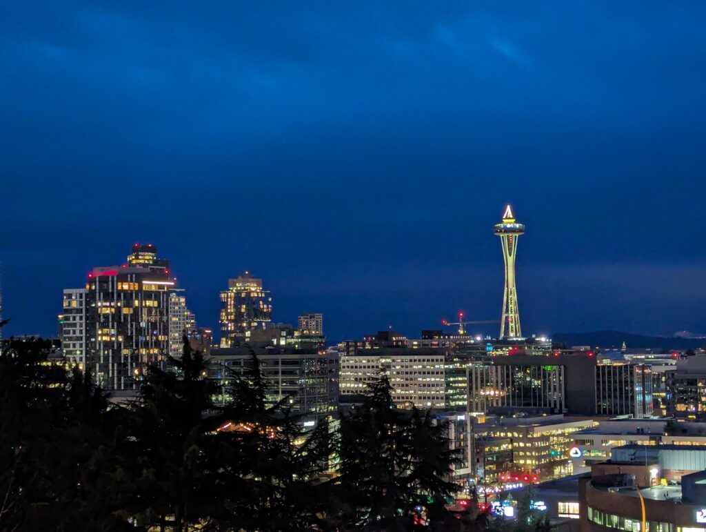 An image of the Seattle skyline in late evening. The space needle stands tall among lit buildings around it.