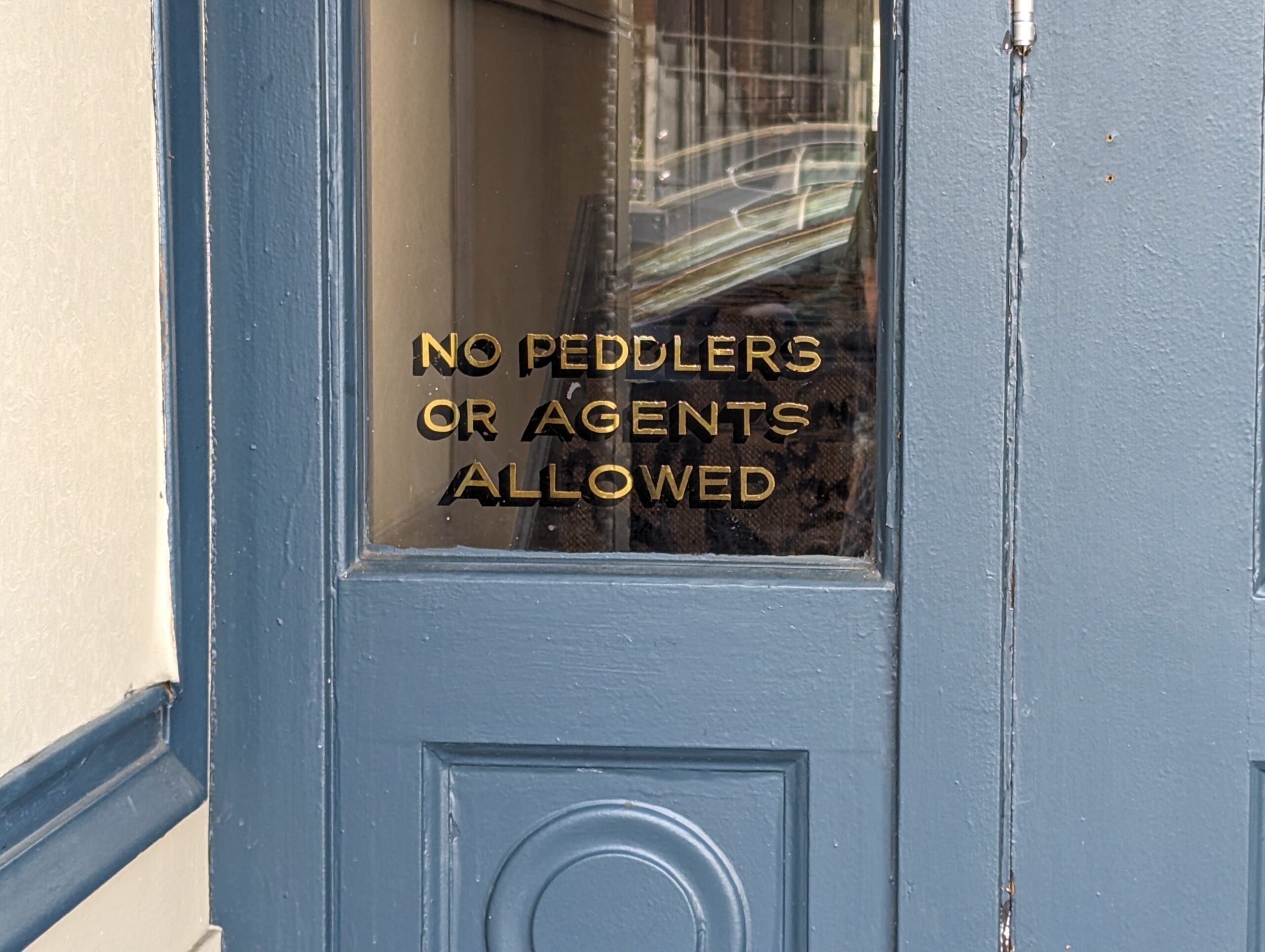 Text printed in a window in gold font that says "No Peddlers or Agents Allowed."